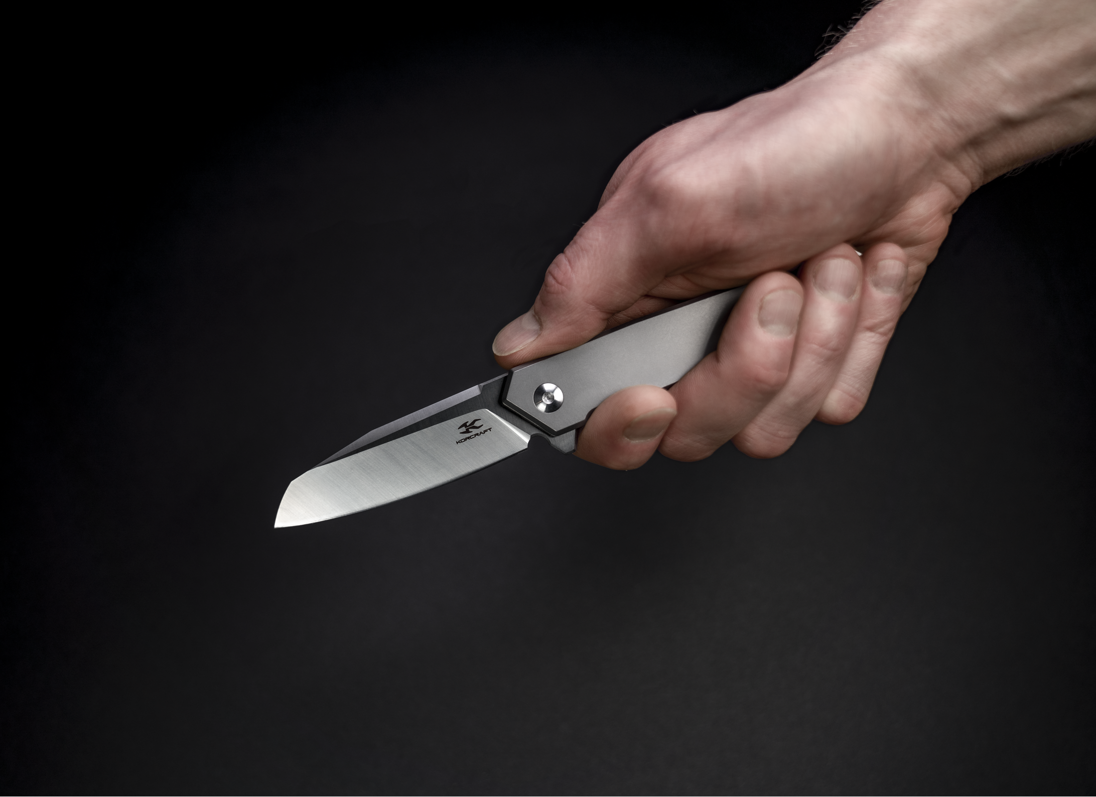 The Rixa by Korcraft, titanium handle and D2 blade open held in the hand on black background